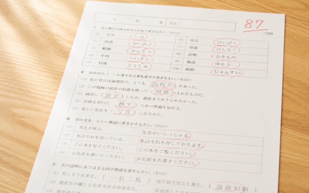 赤ペンで採点された答案用紙。×より○が多めで、惜しい点数のイメージ。机の上に置かれている画像